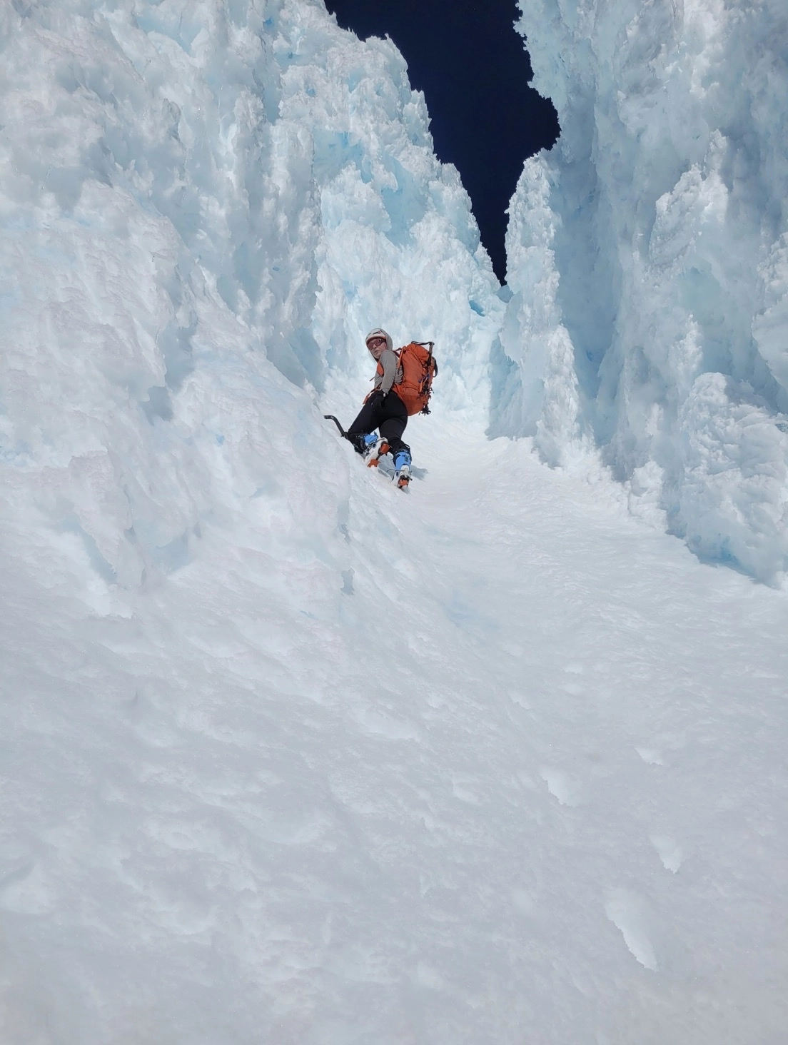 Ice climber ascending frozen waterfall canyon with blue-white ice formations