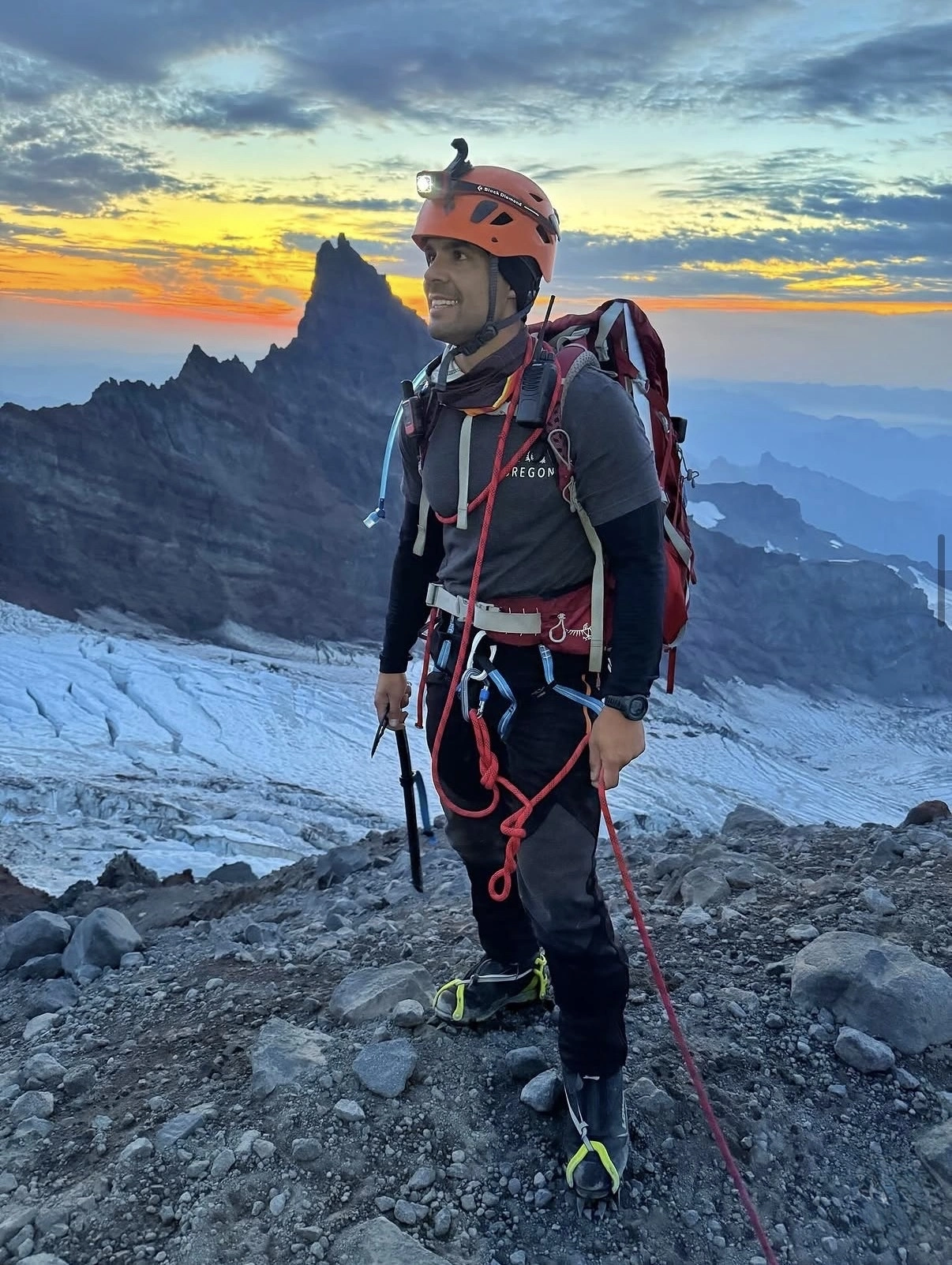 Luis Gil in climbing gear with orange helmet and harness on alpine terrain at sunset