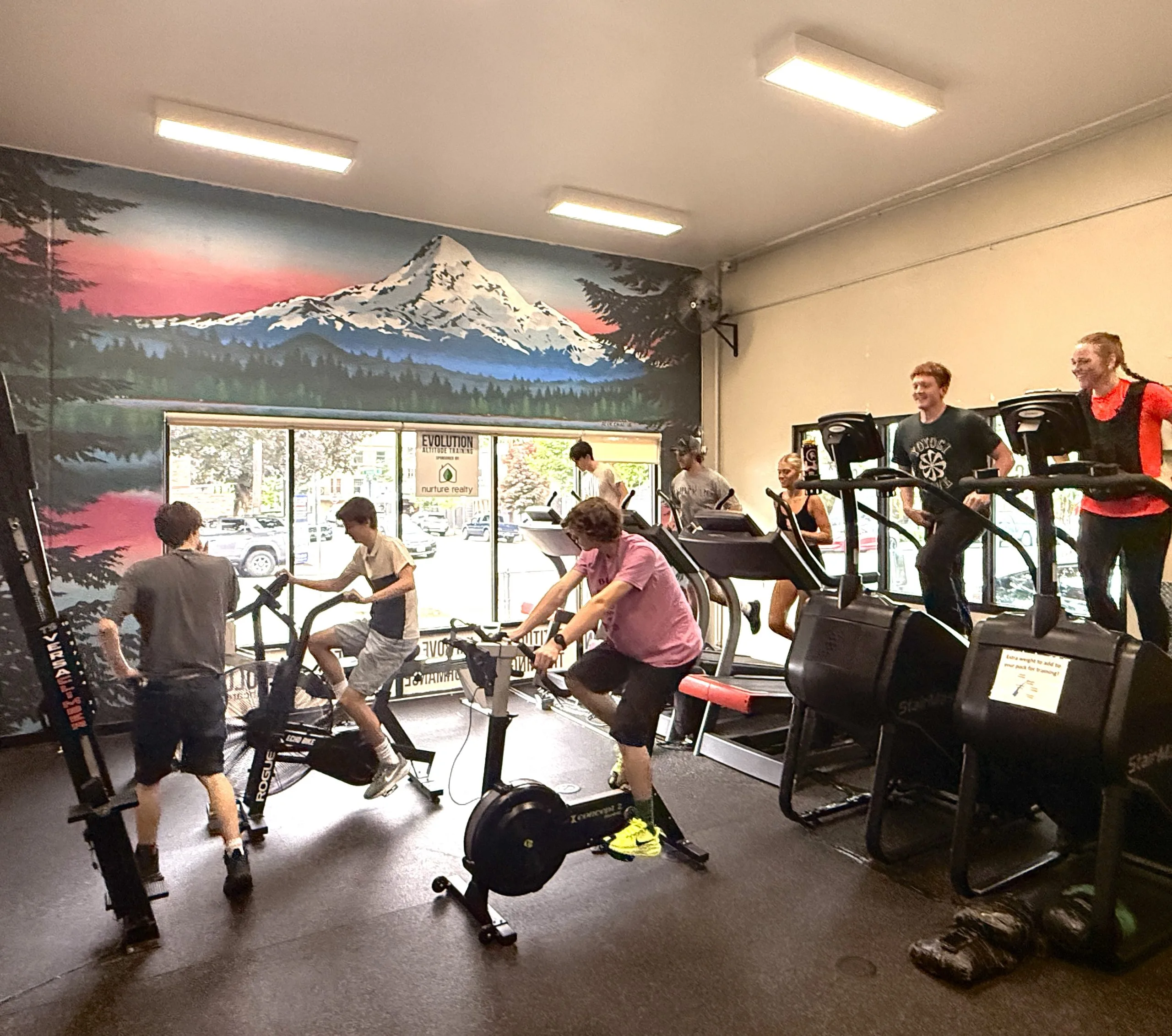 Group fitness class with multiple people on stationary bikes in a gym with mountain mural