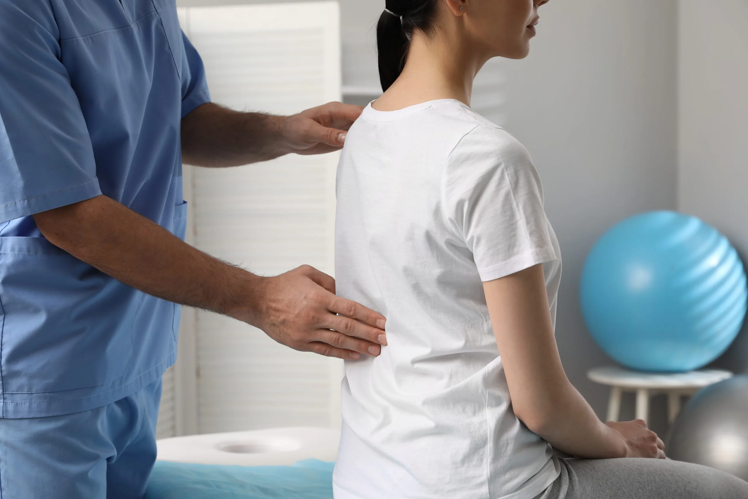 Chiropractor in blue scrubs palpating patient's spine and posture during examination in clinic