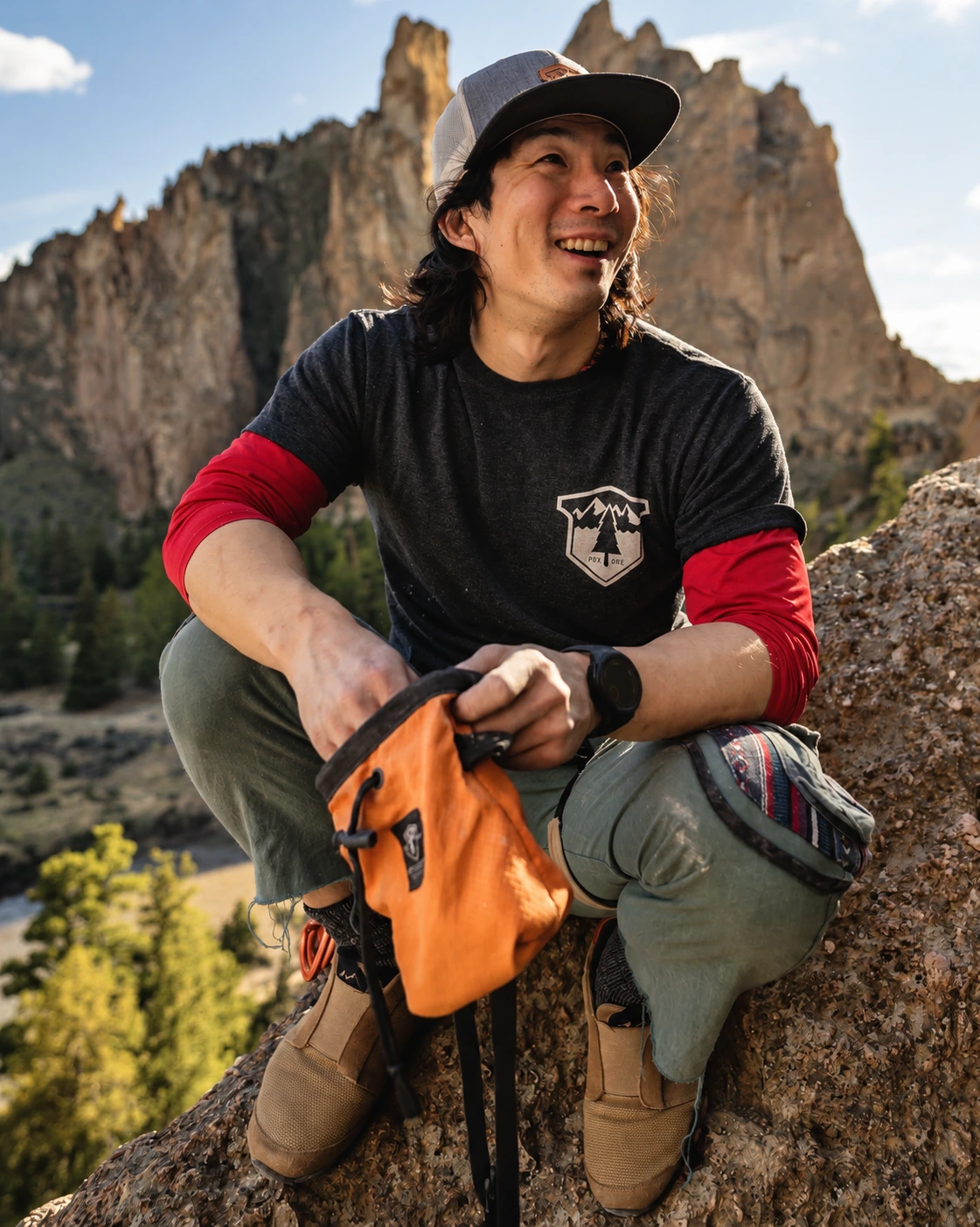 Ju Kim sitting on a rock with climbing gear, smiling, mountain landscape in the background