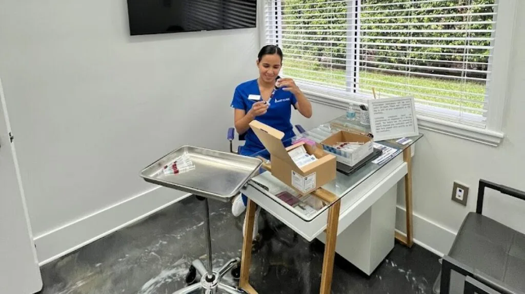 Staff member in blue shirt preparing injectable supplies at clinical workstation