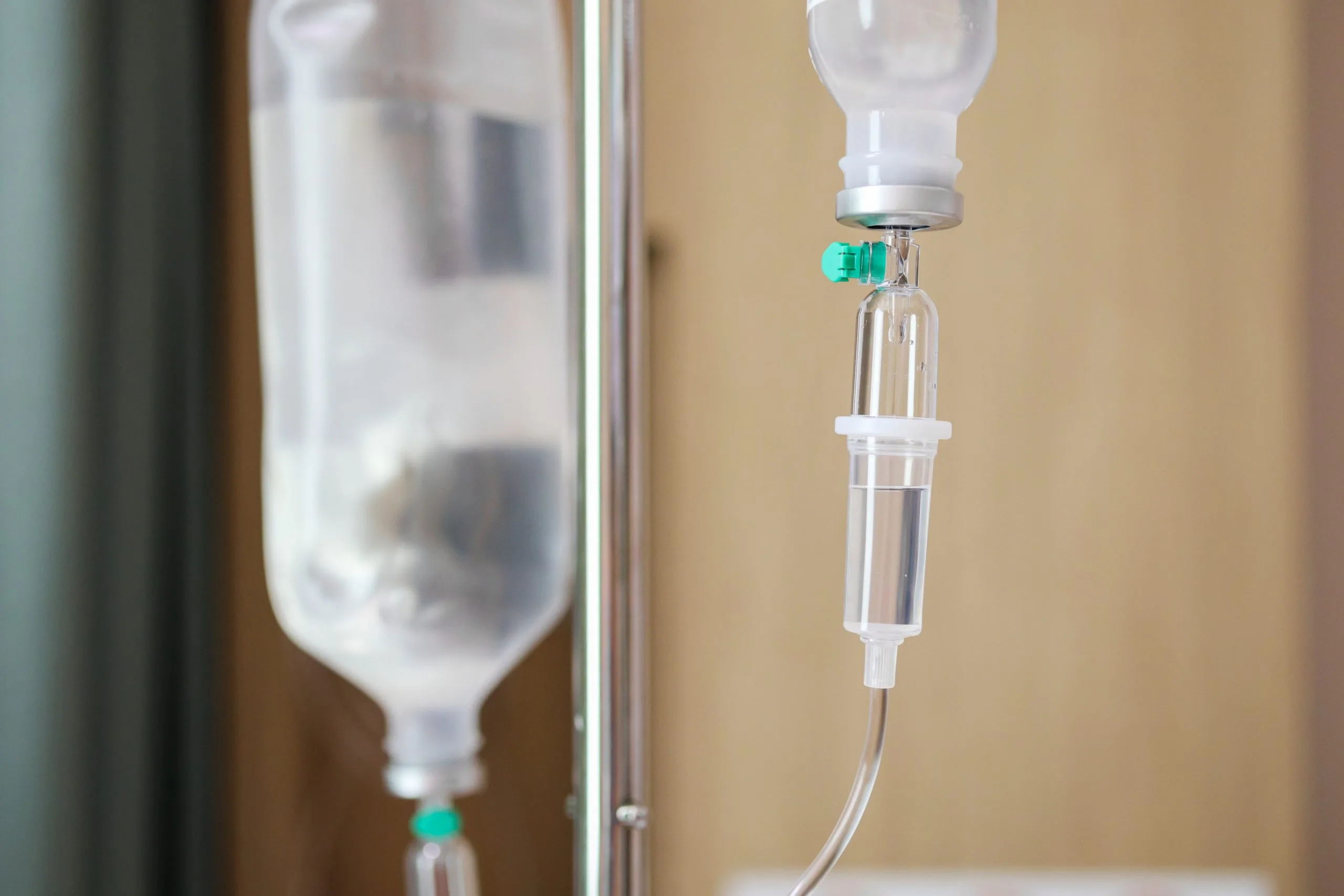 Intravenous drip bag and tubing with green valve against neutral medical background