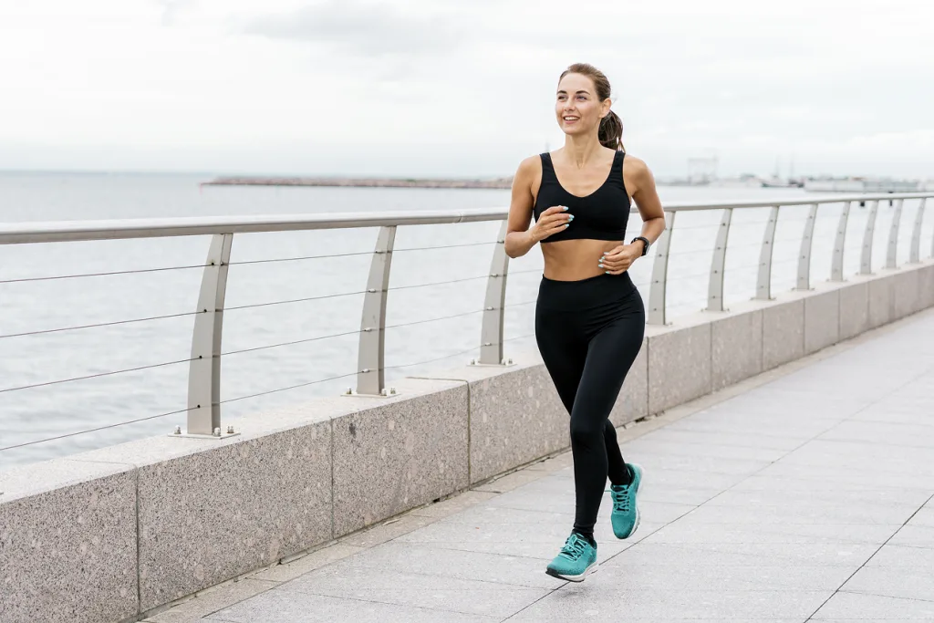 Woman jogging along a waterfront path while checking her smartwatch
