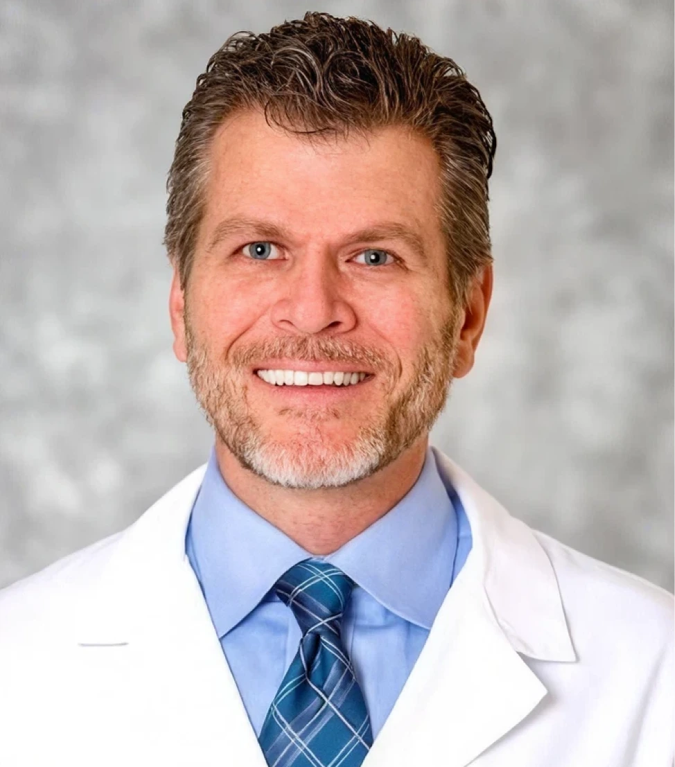 Joseph Gauta, MD, URPS, headshot portrait in white medical coat and blue shirt