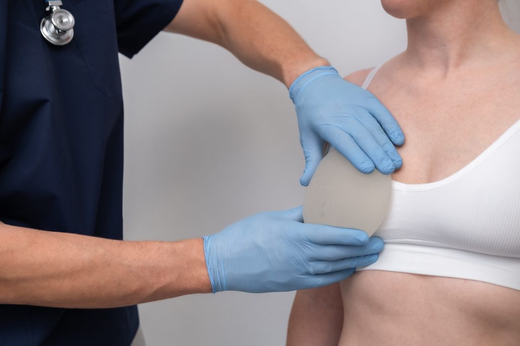 Surgeon in blue gloves examining patient's chest during breast augmentation consultation