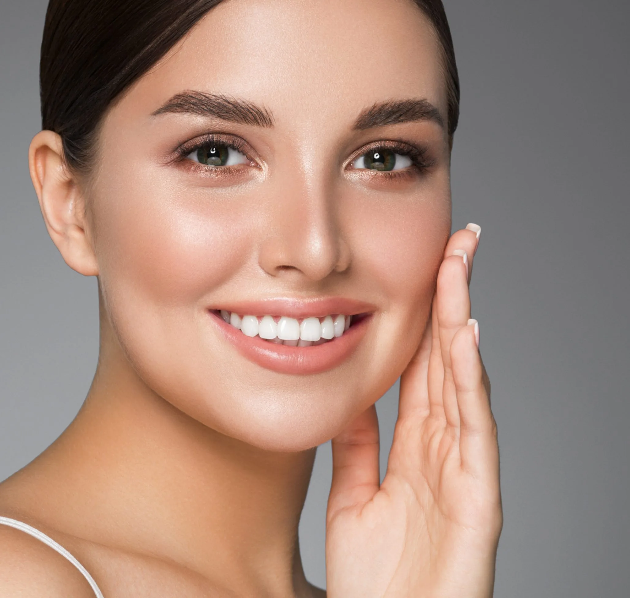 Woman touching face with bright smile and clear skin against gray background