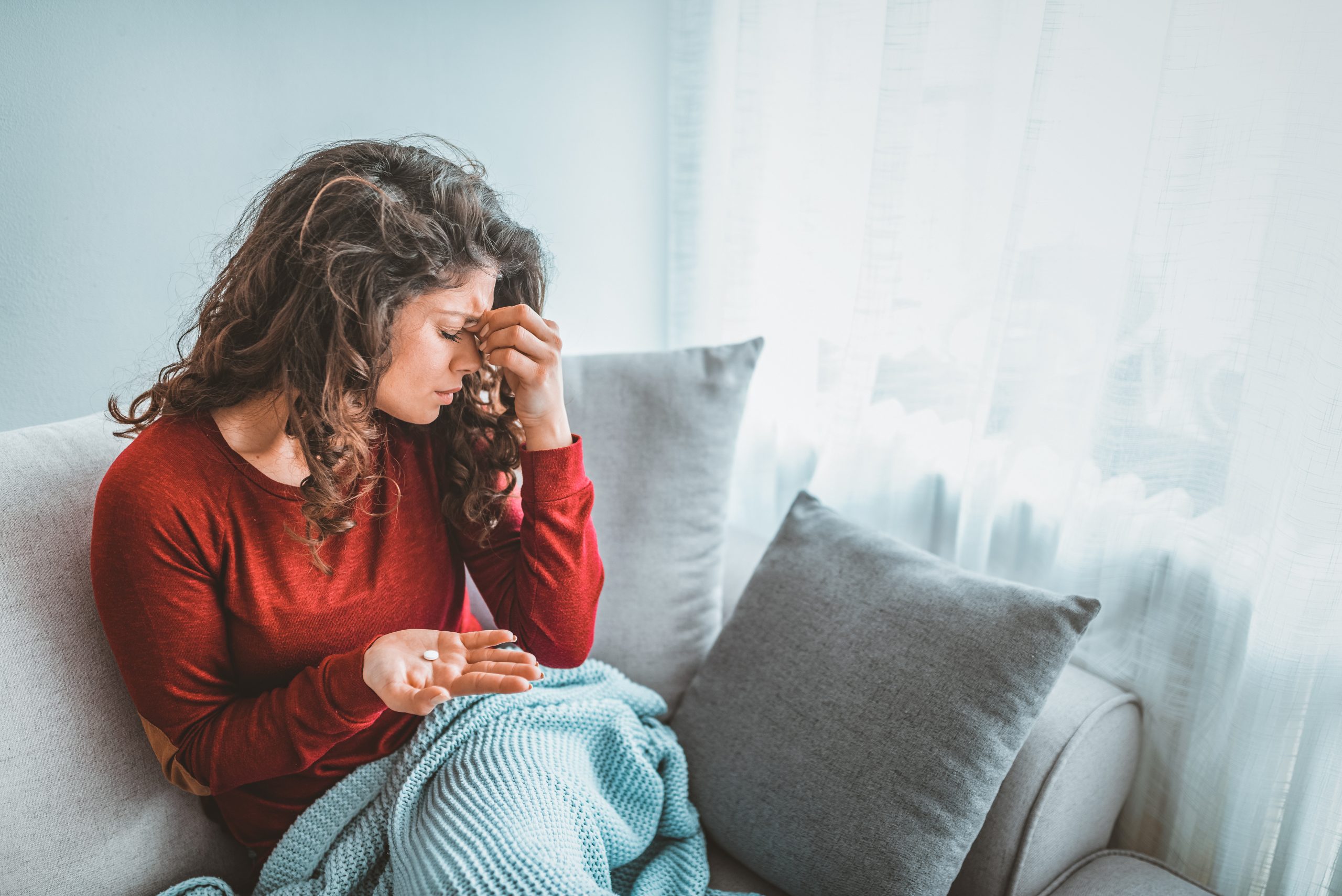 Woman in red sweater sitting on couch holding head, appearing distressed