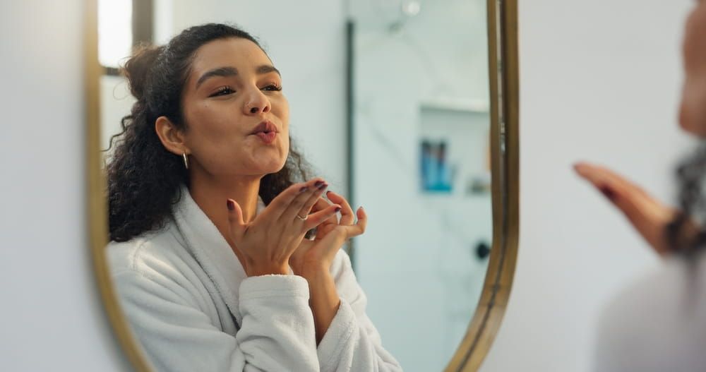 Woman examining her face in mirror with hands near cheeks