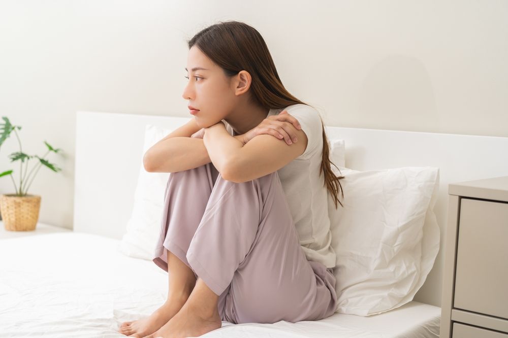 Woman sitting on bed hugging her knees, looking unwell