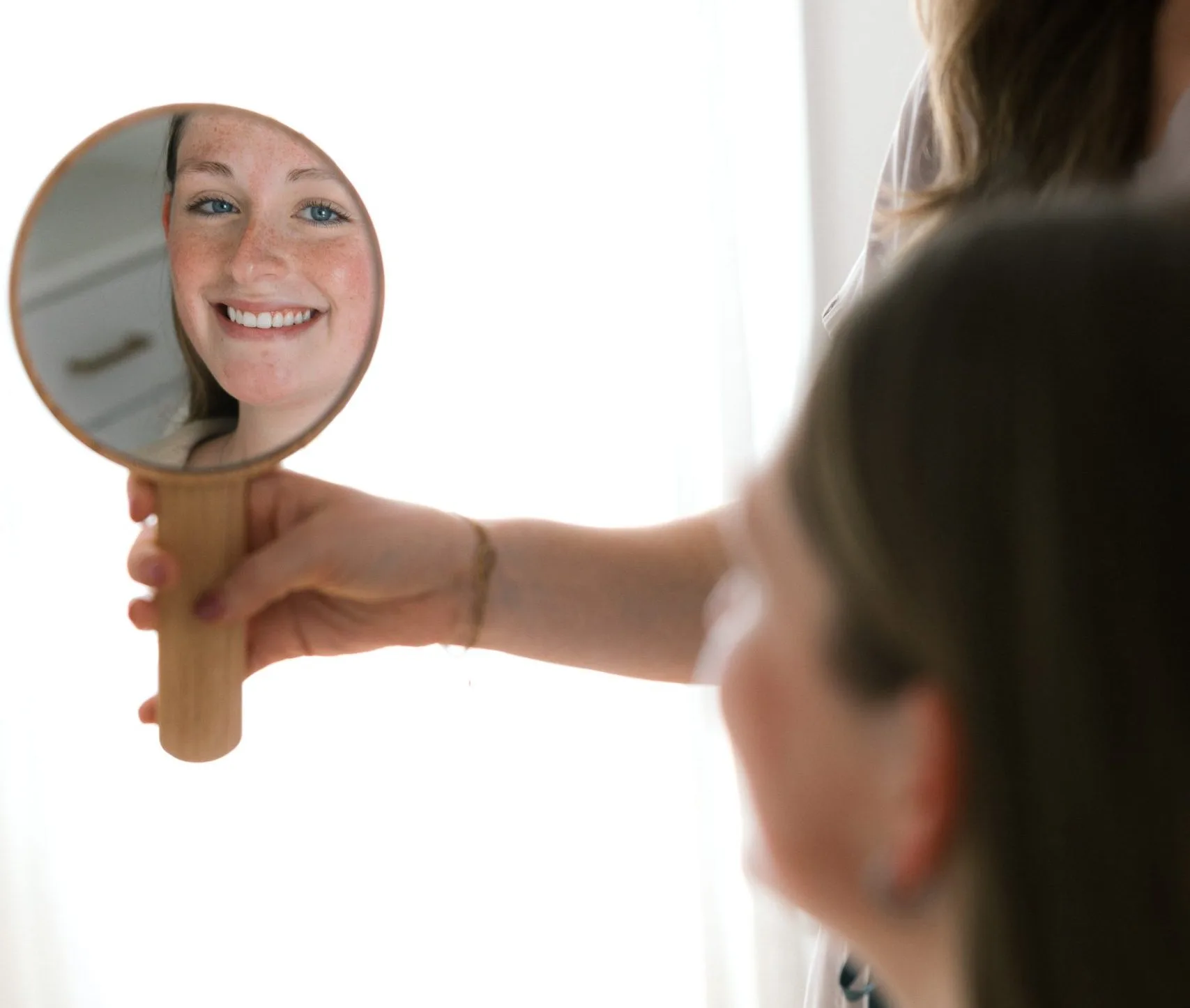 Woman smiling at her reflection in a hand mirror