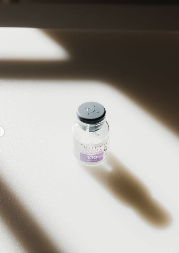 Botox vial with purple label and black cap on white surface in natural light
