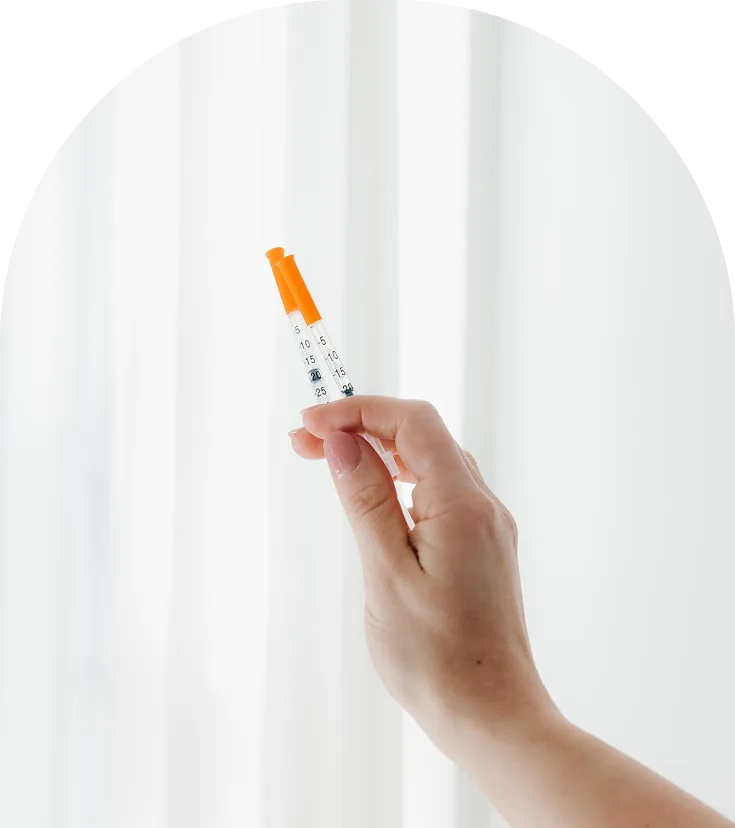 Hand holding injectable syringe with orange plunger and measurement markings