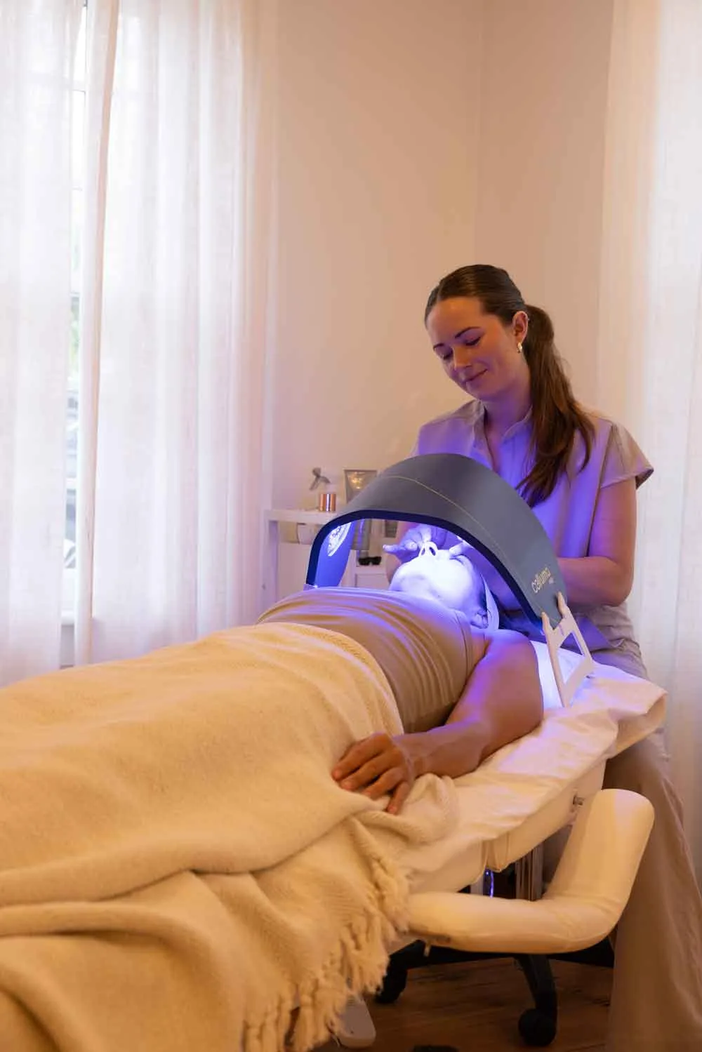 Esthetician using LED light therapy device on patient's face during facial procedure