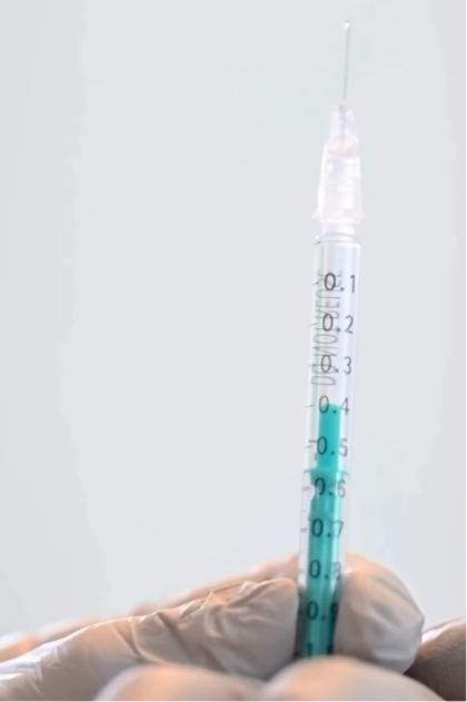 Gloved hand holding a syringe filled with teal injectable solution marked with measurement graduations