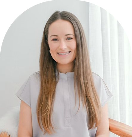 Kelsey, a woman with long brown hair wearing a light gray shirt, smiling in a bright clinical setting