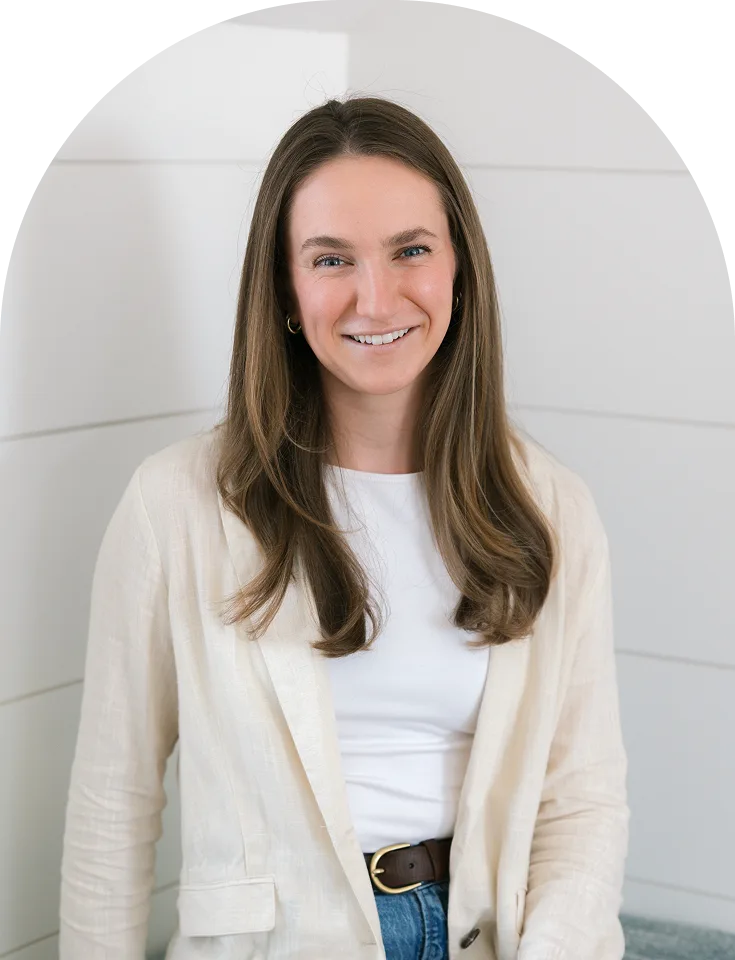 Woman with long brown hair smiling, wearing cream cardigan over white top and jeans