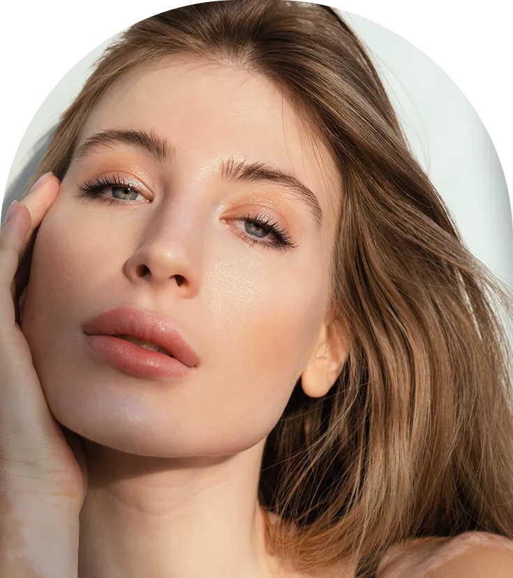 Woman with brown hair touching her face, displaying smooth, radiant skin