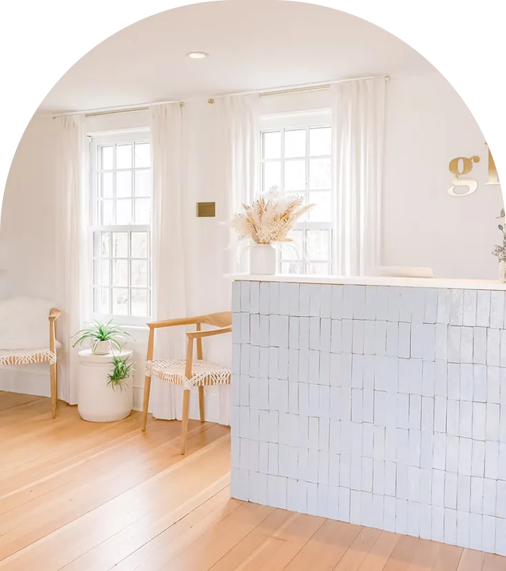 Bright medical reception area with white tile desk, wooden chairs, and large windows