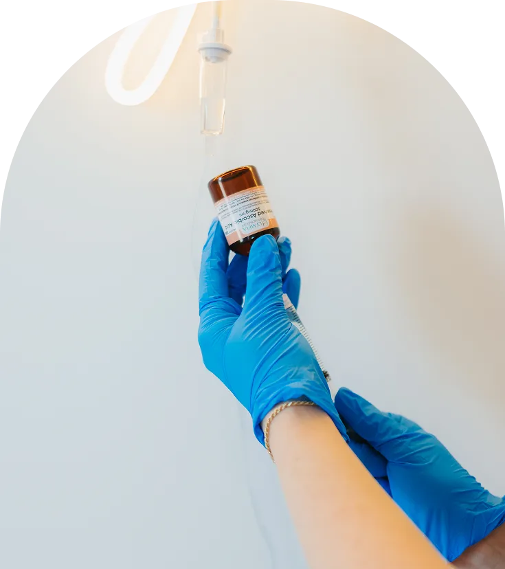 Gloved hand holding amber vial with syringe above, preparing injectable treatment