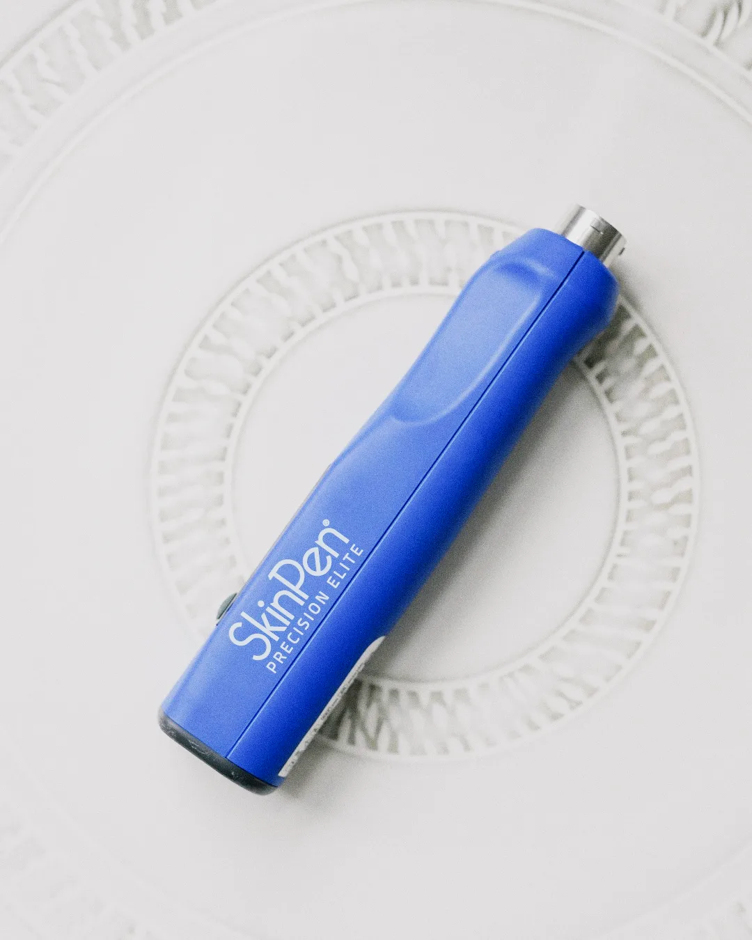 SkinPen microneedling device in blue with silver accents on white textured background