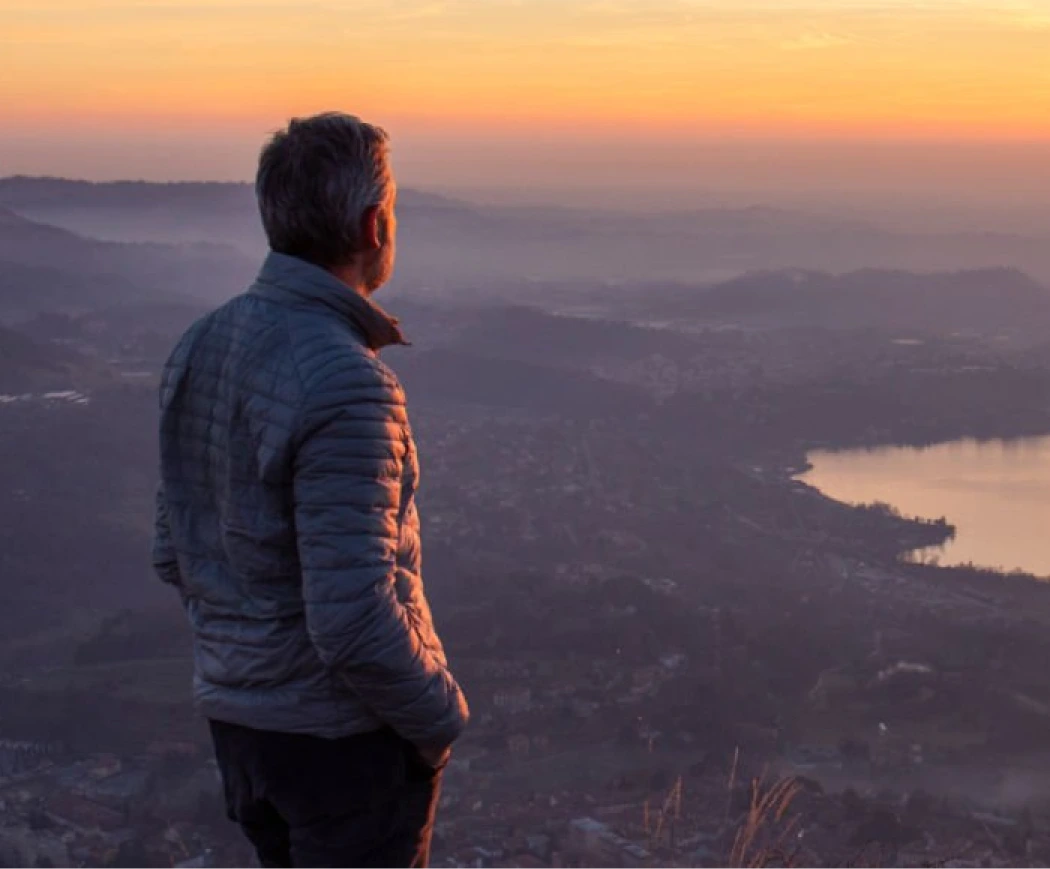 Person standing on a hilltop overlooking a misty valley landscape at sunset