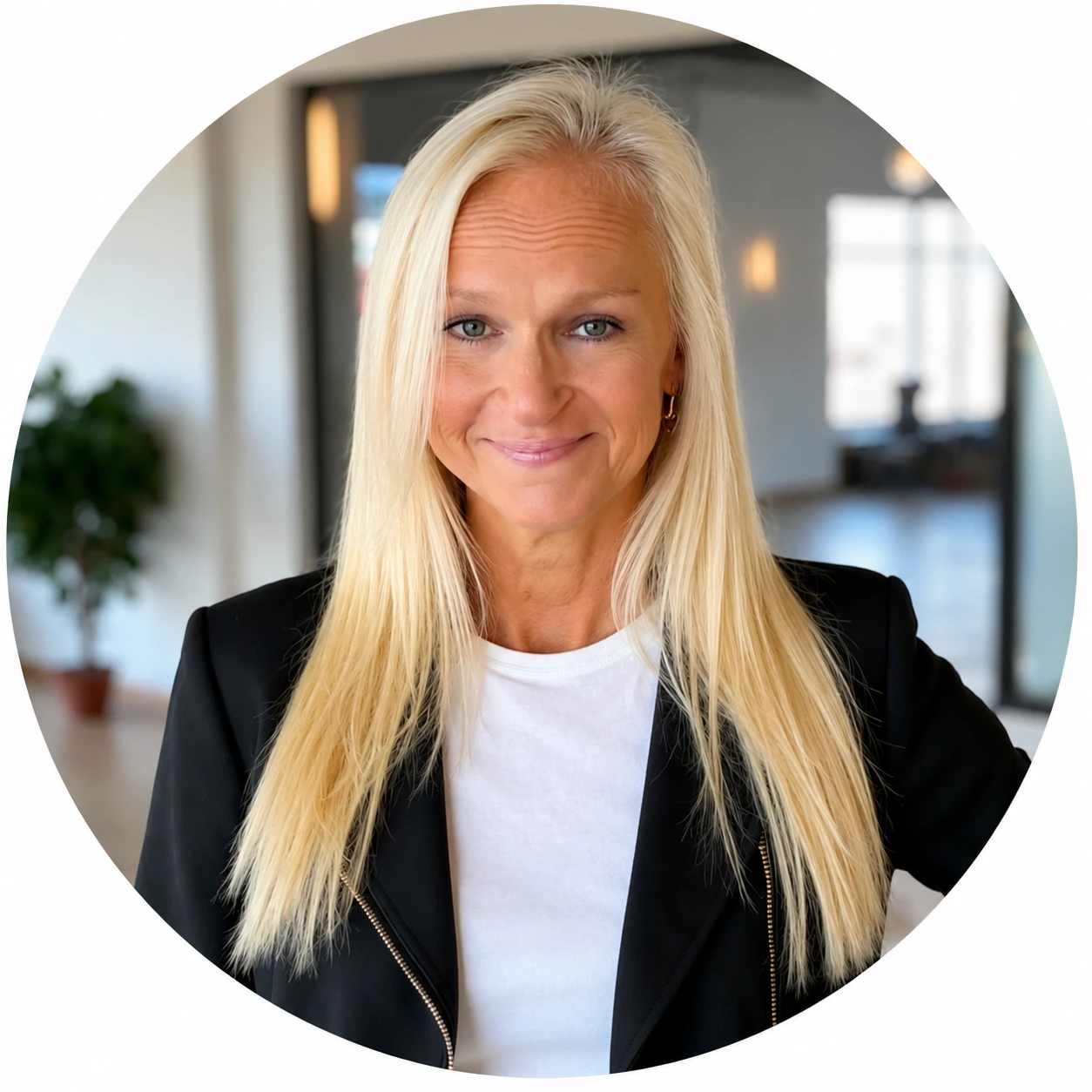 Woman with blonde hair wearing black blazer and white shirt, smiling in modern office setting