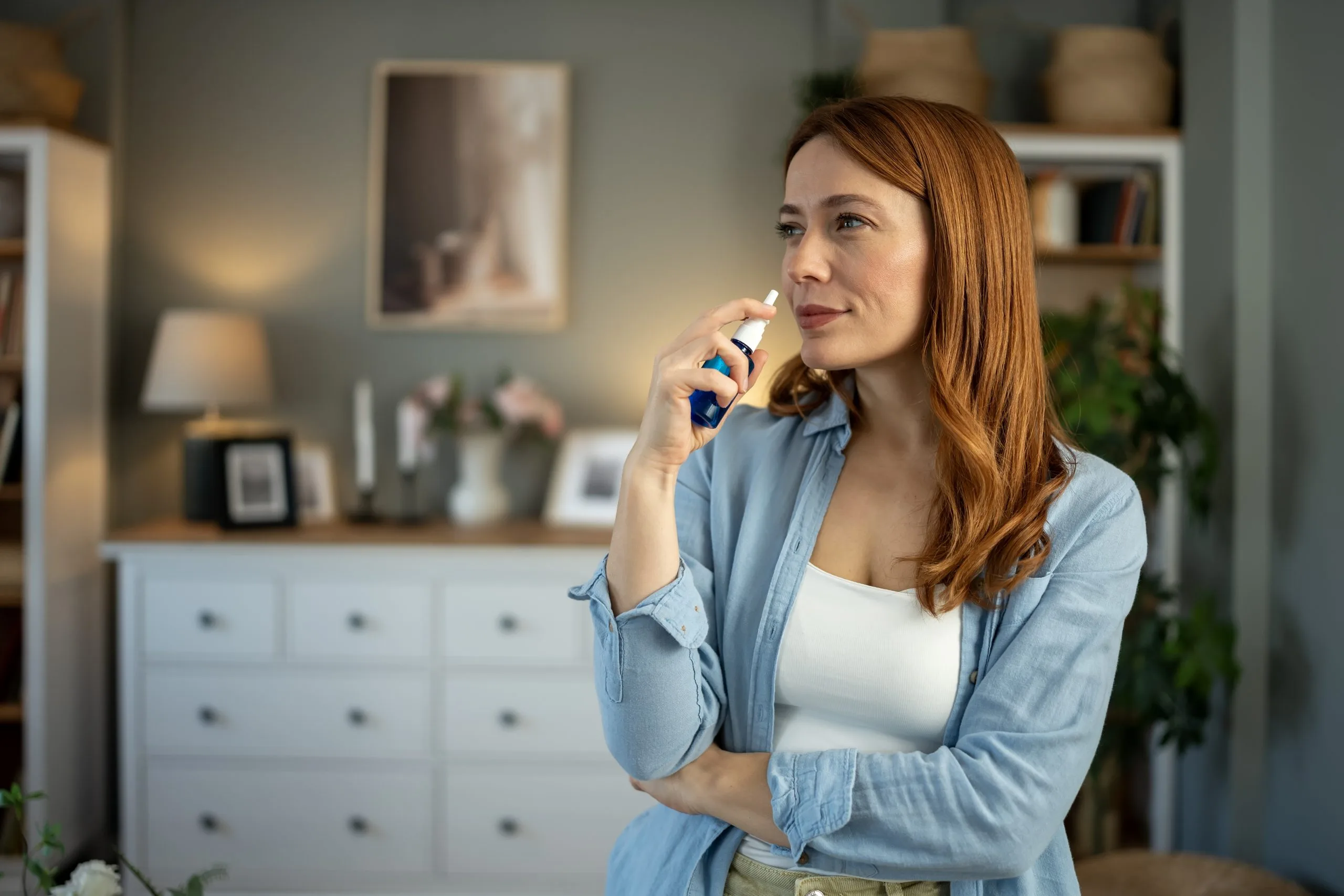 Woman with reddish-brown hair speaking on a blue phone in a bright home office with shelving and plants