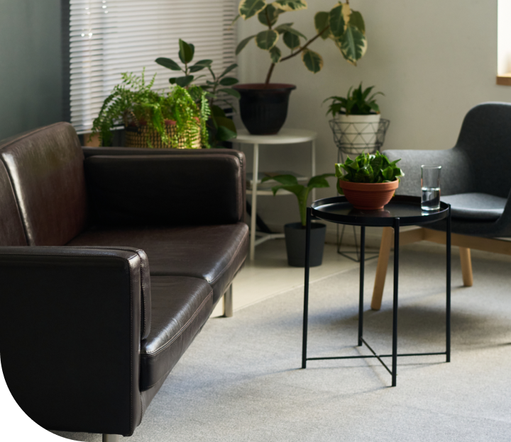 Modern waiting room with brown leather seating, potted plants, and small side table