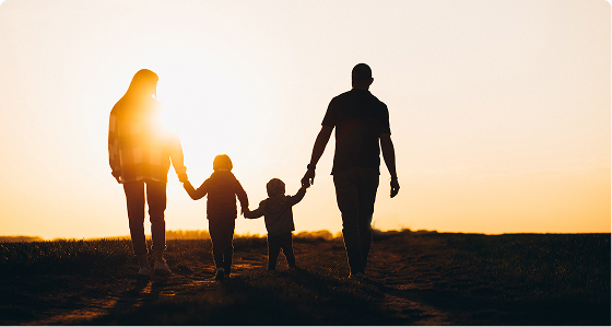 Two adults and two children holding hands walking together at sunset