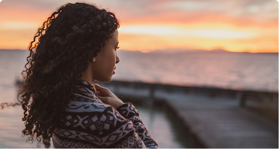 Woman with curly hair looking toward ocean at sunset from a pier