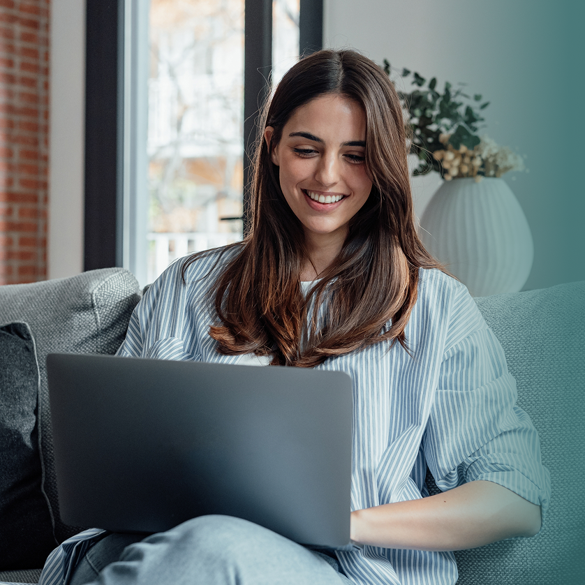 Woman smiling while using a laptop on a couch in a modern living room