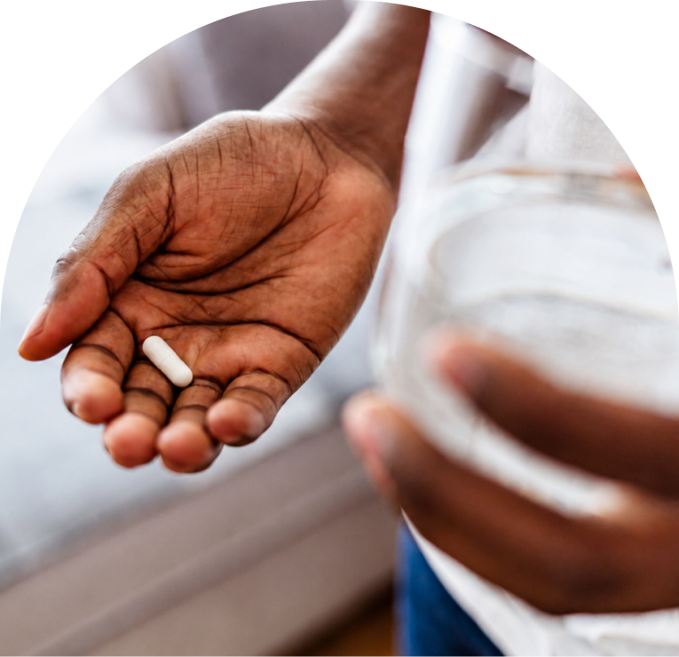 Person holding two white pills in palm with medication bottle in background