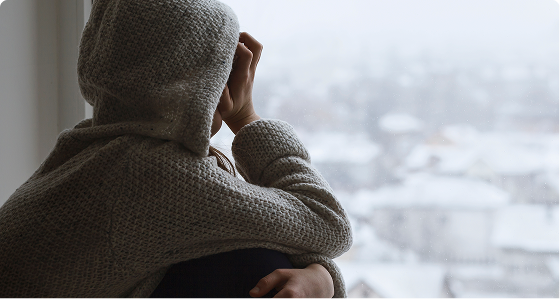 Person from behind wearing gray sweater, looking out window at snowy cityscape