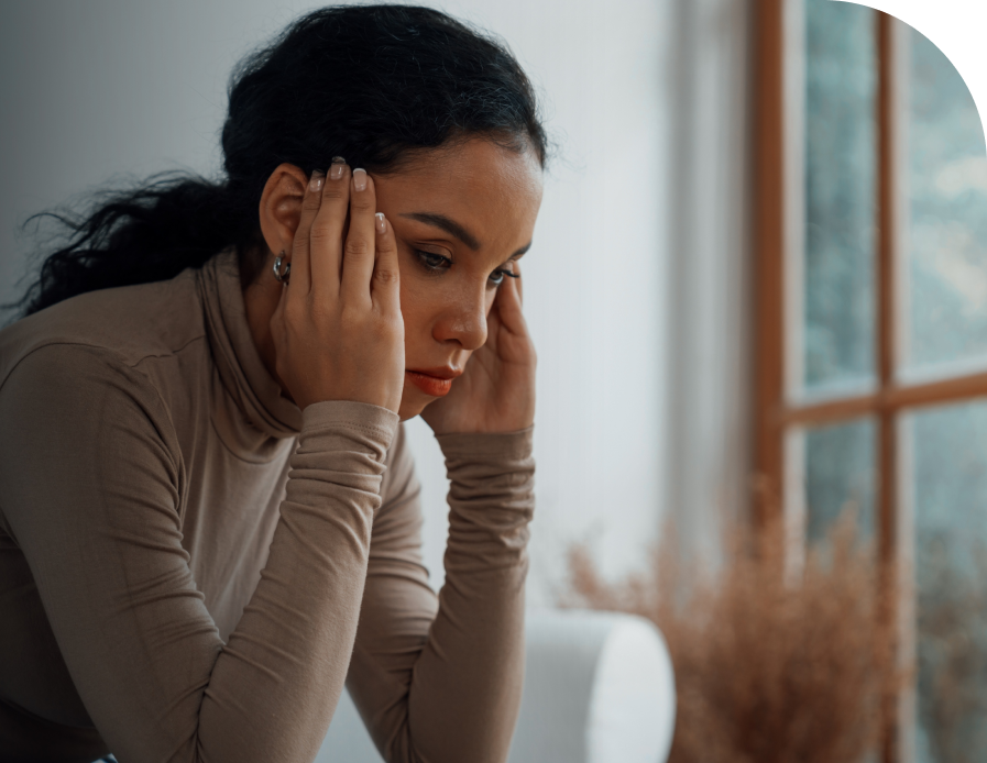 Woman with head in hands looking distressed, sitting by a window
