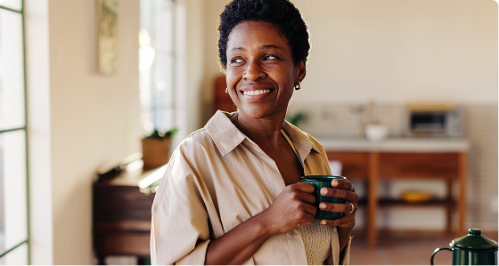 Smiling woman in tan shirt holding a mug in a bright home setting
