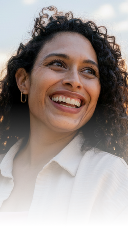 Woman with curly dark hair smiling outdoors wearing a white shirt