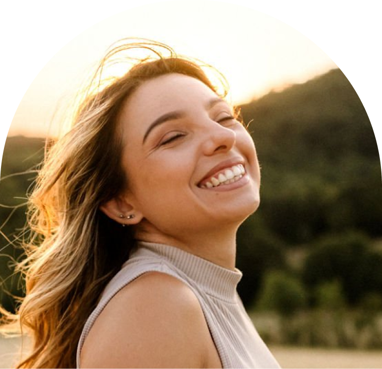 Woman smiling outdoors in golden sunlight with blurred green background