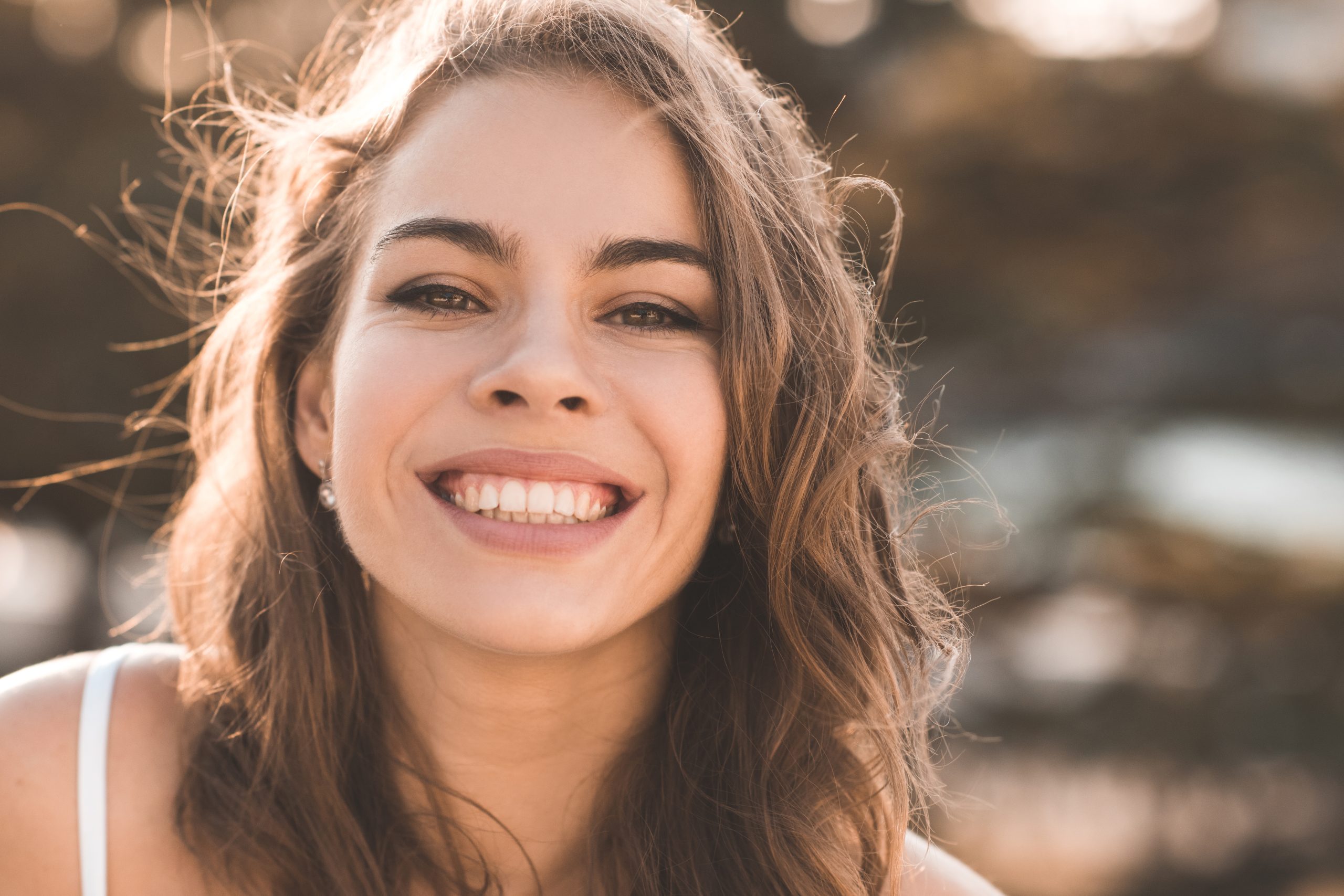 Woman with wavy brown hair smiling brightly in golden hour light