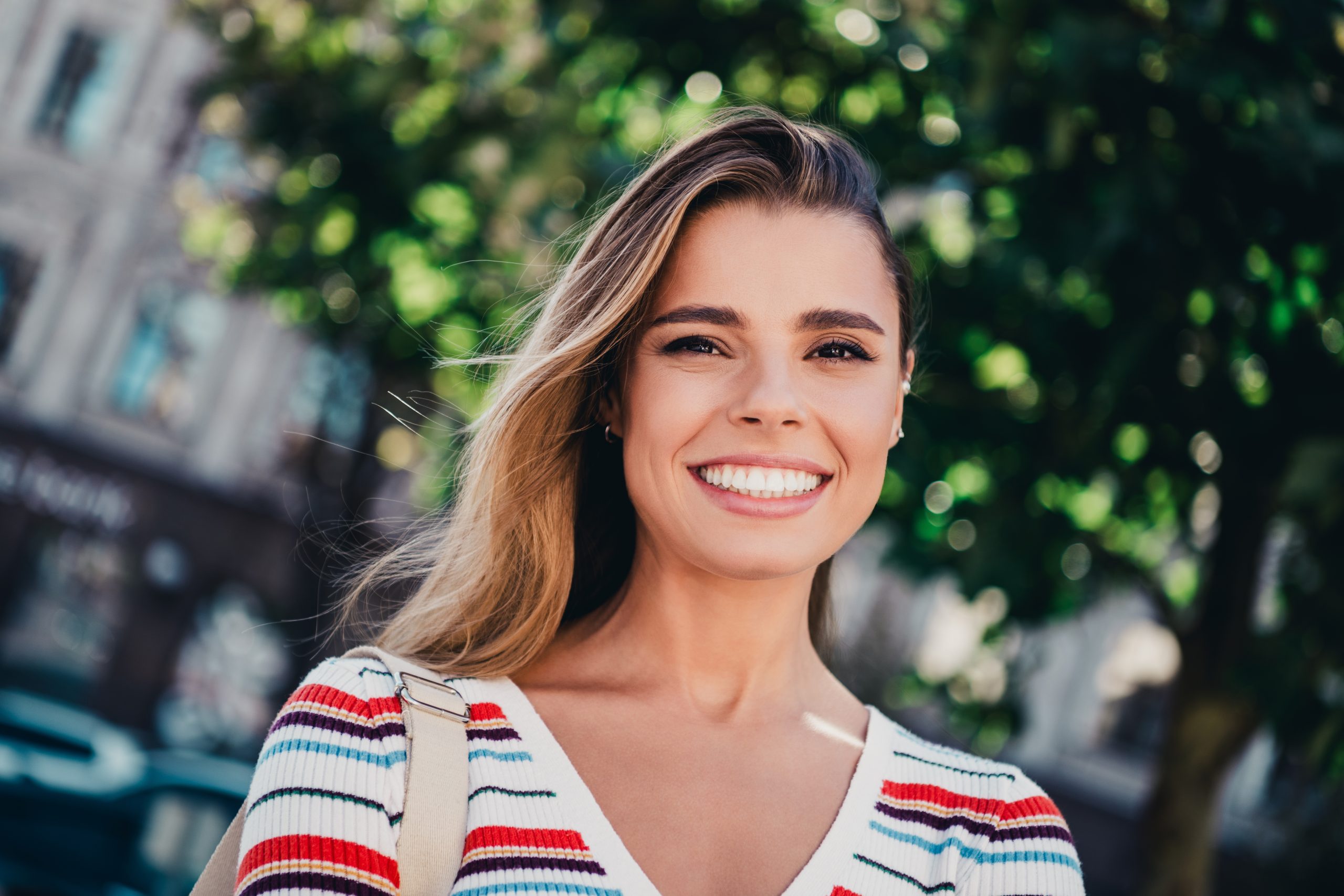 Woman in striped red and blue top smiling outdoors with greenery behind