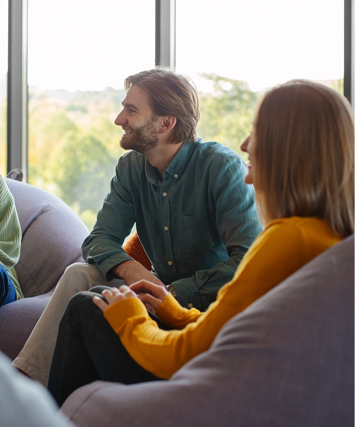 Two adults engaged in conversation during a group support meeting by a bright window