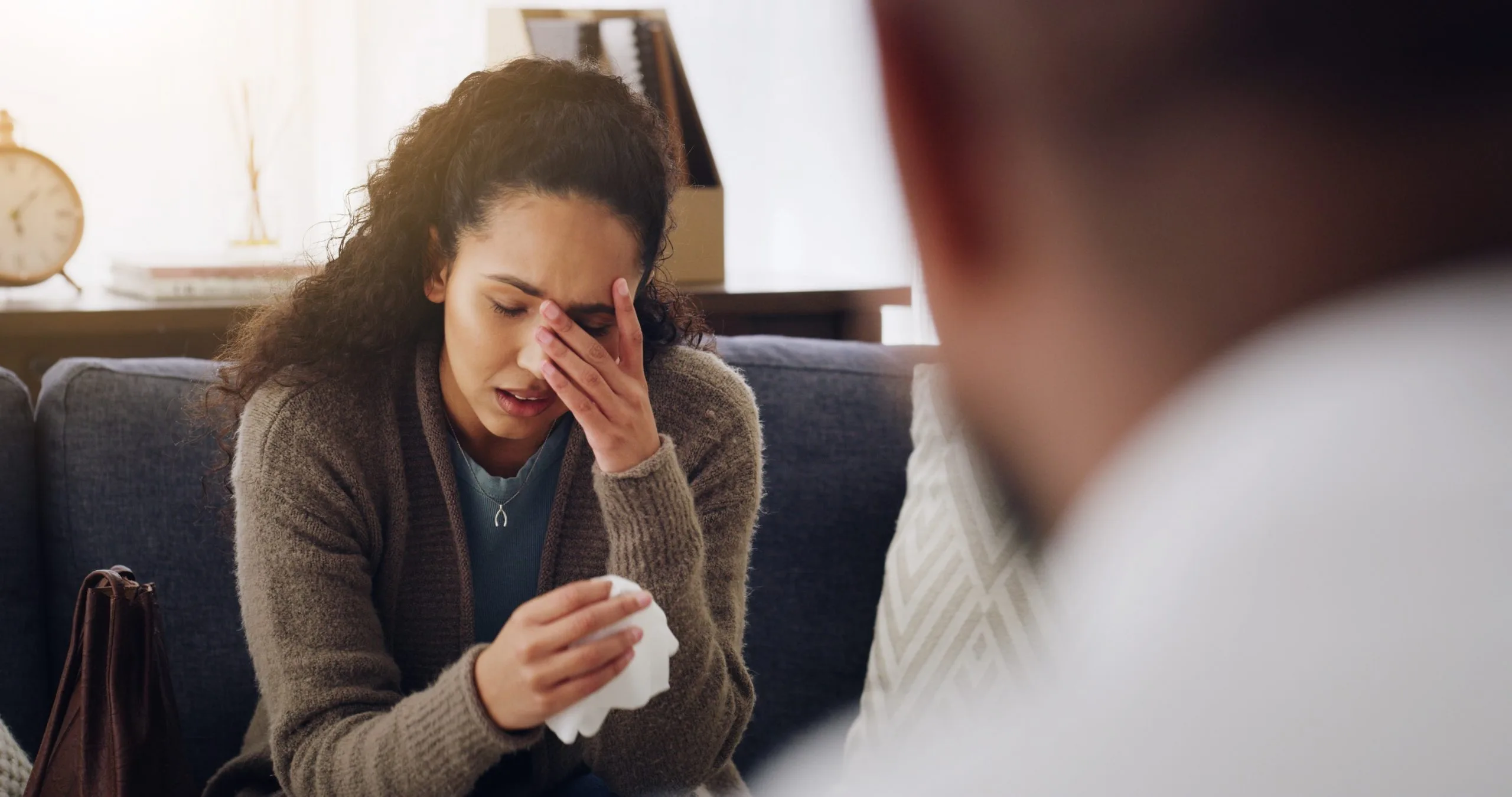 Woman in therapy session holding tissue and touching her face while speaking with counselor