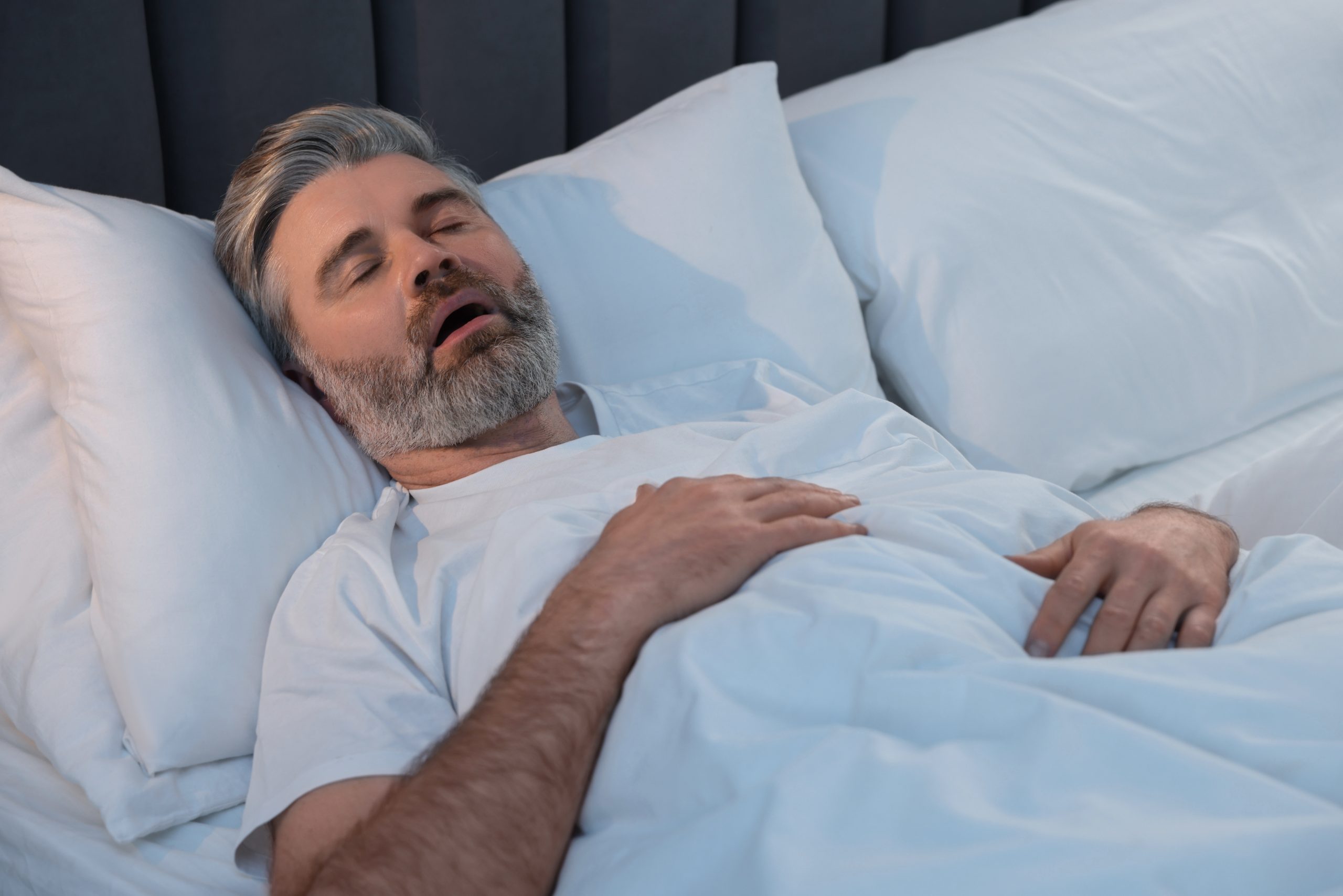 Middle-aged man sleeping in bed with mouth open, illustrating sleep apnea symptoms