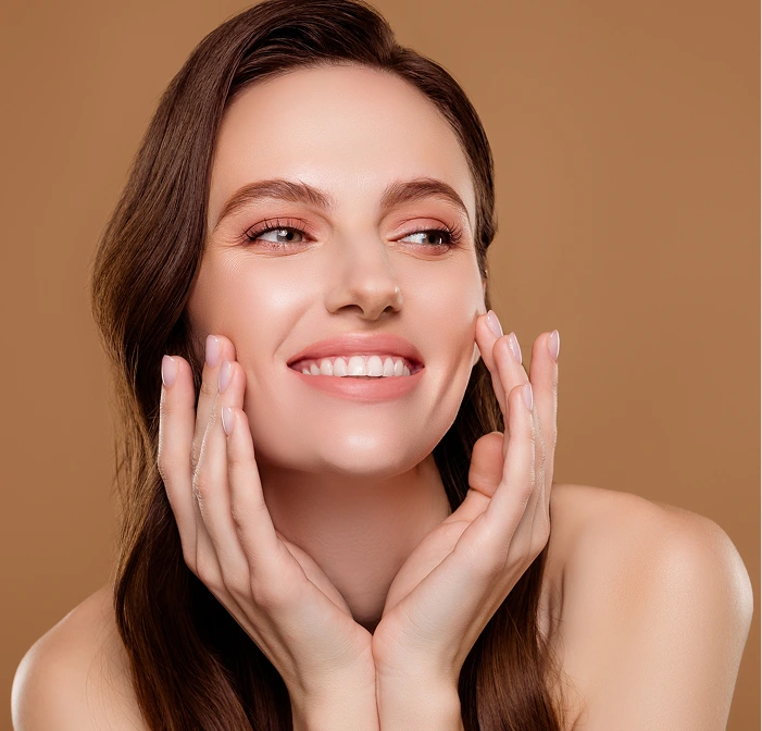 Woman with dark hair smiling and cupping her face with hands against tan background