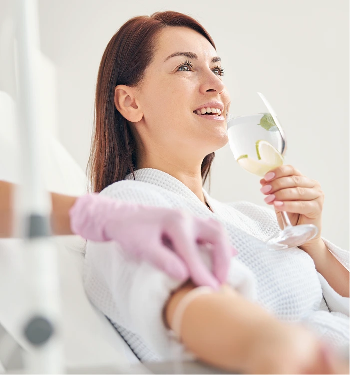 Woman in white towel holding glass of infused water, smiling