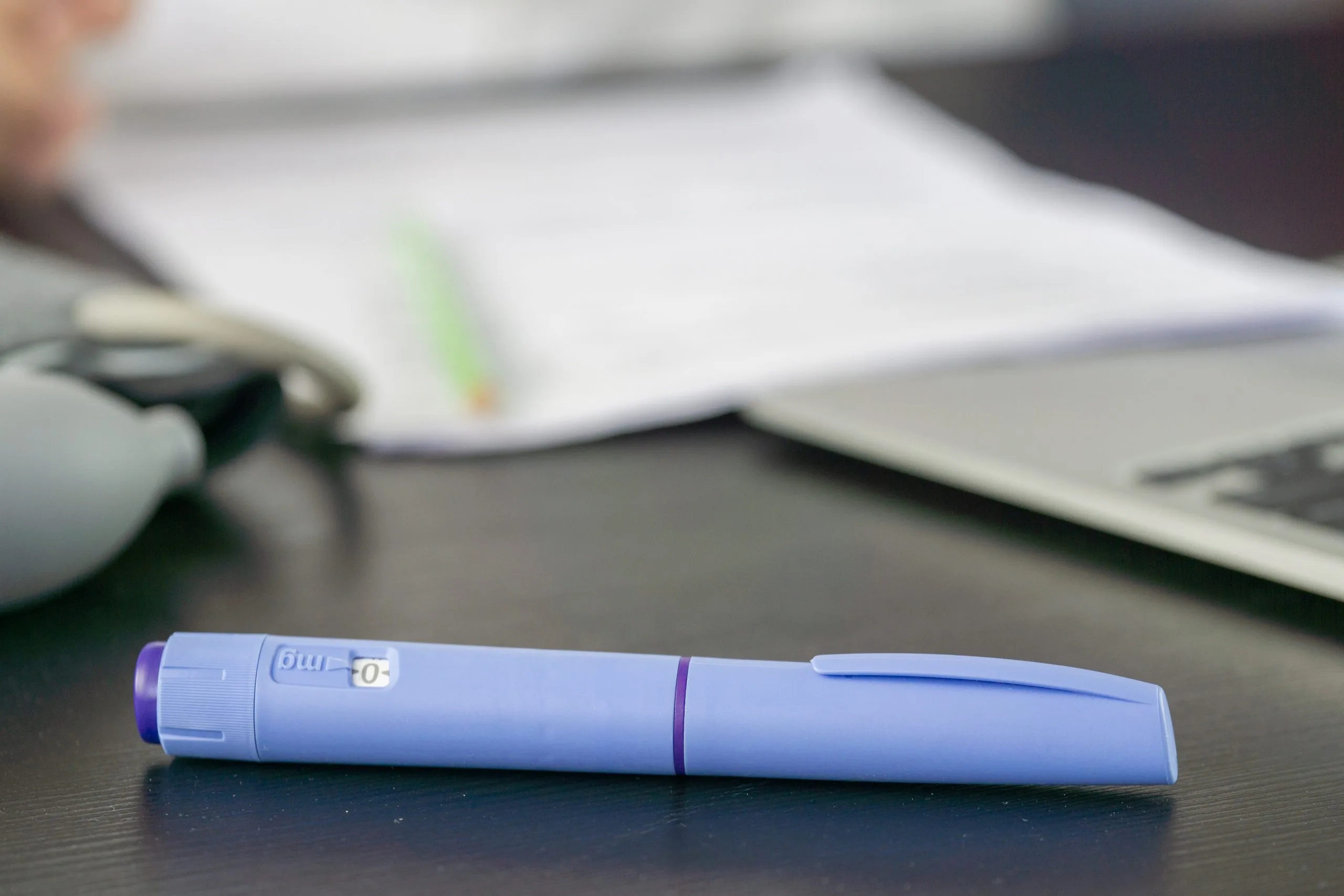Blue injectable pen on desk with computer mouse and papers in background