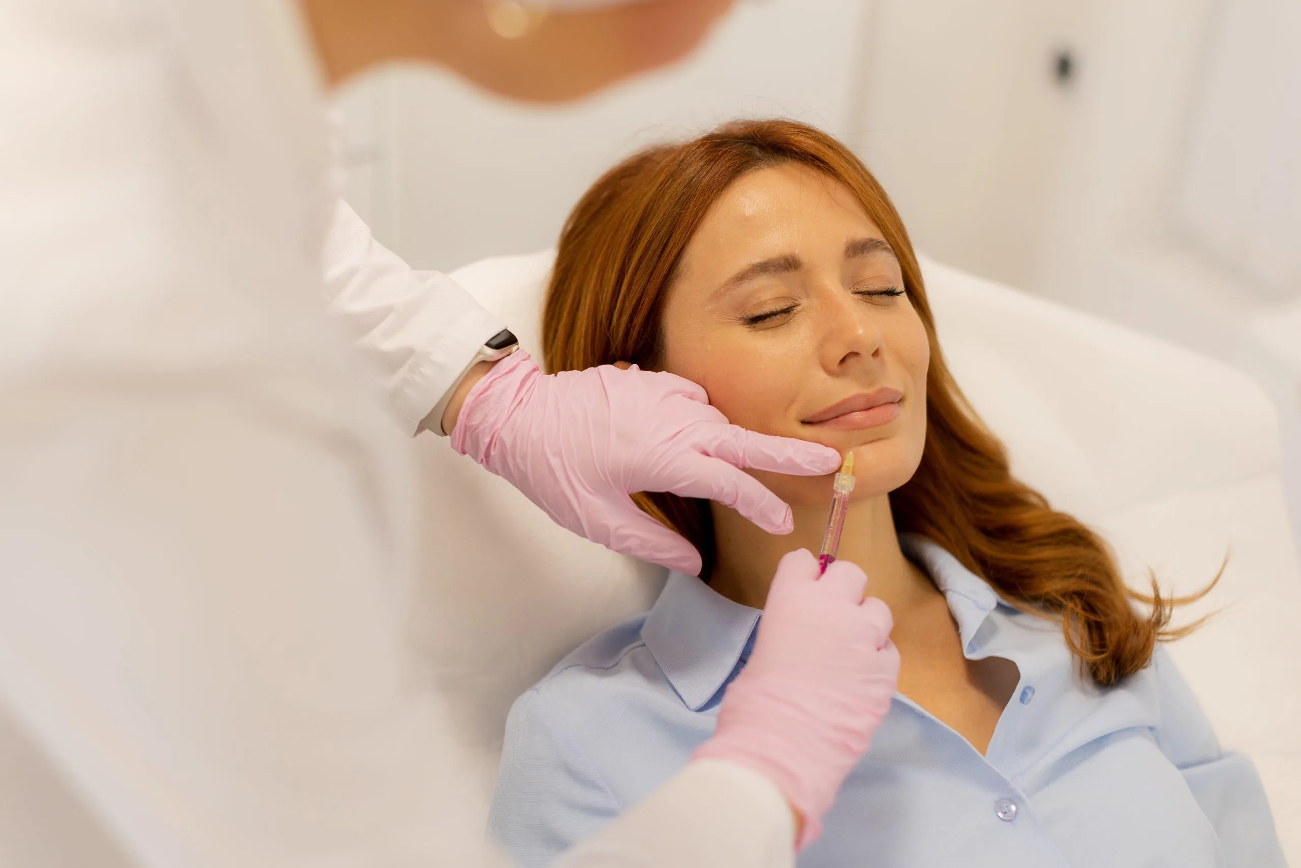 Practitioner in pink gloves administering lip filler injection to relaxed client