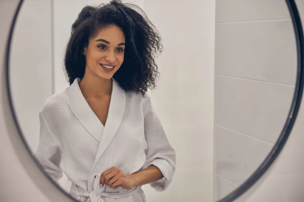 Woman in white robe smiling in round mirror