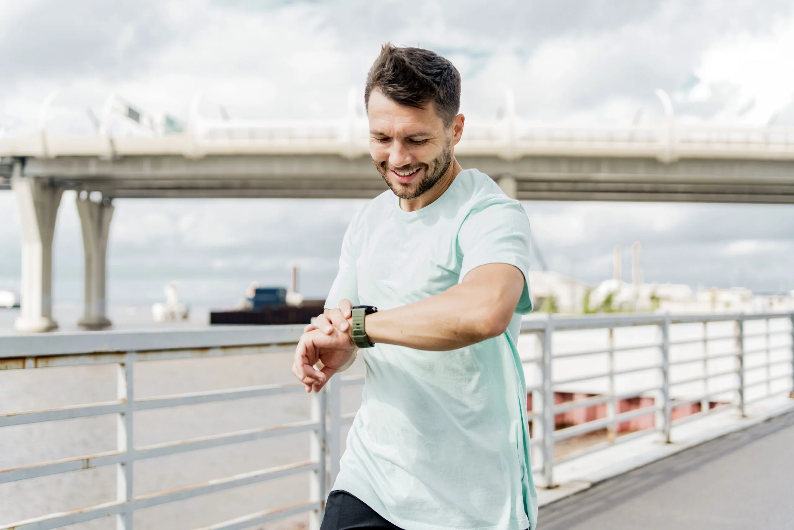 Man jogging on a waterfront path checks his fitness watch