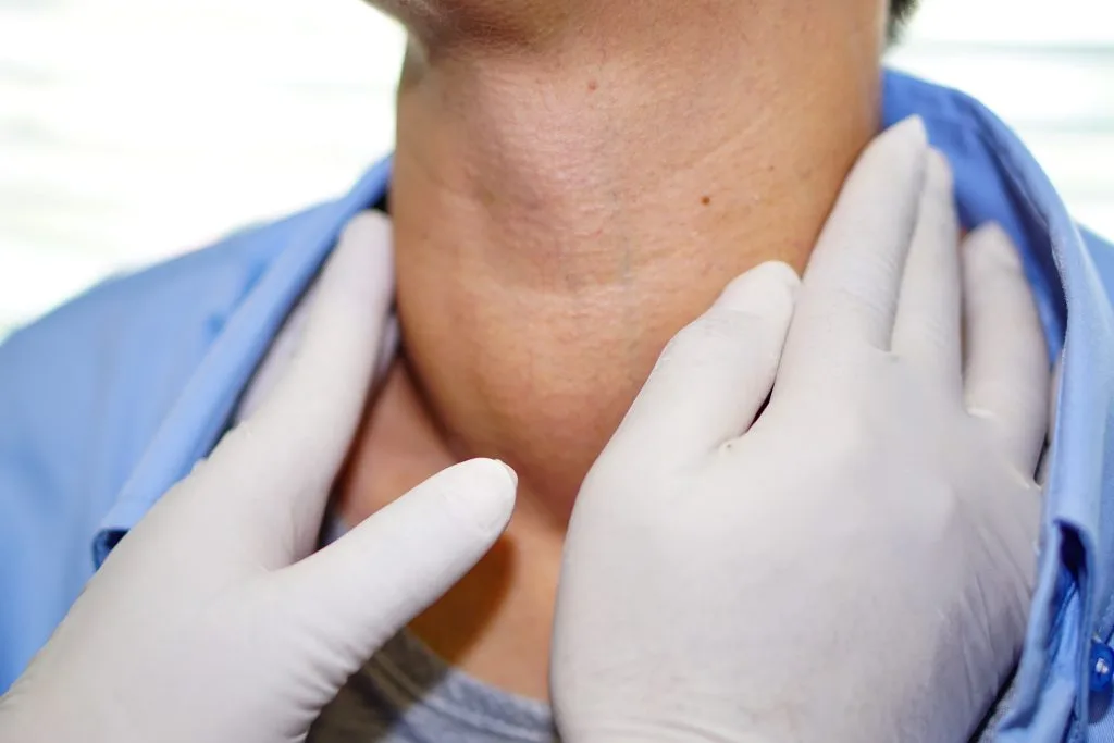 Doctor in blue coat palpating patient's neck with gloved hands